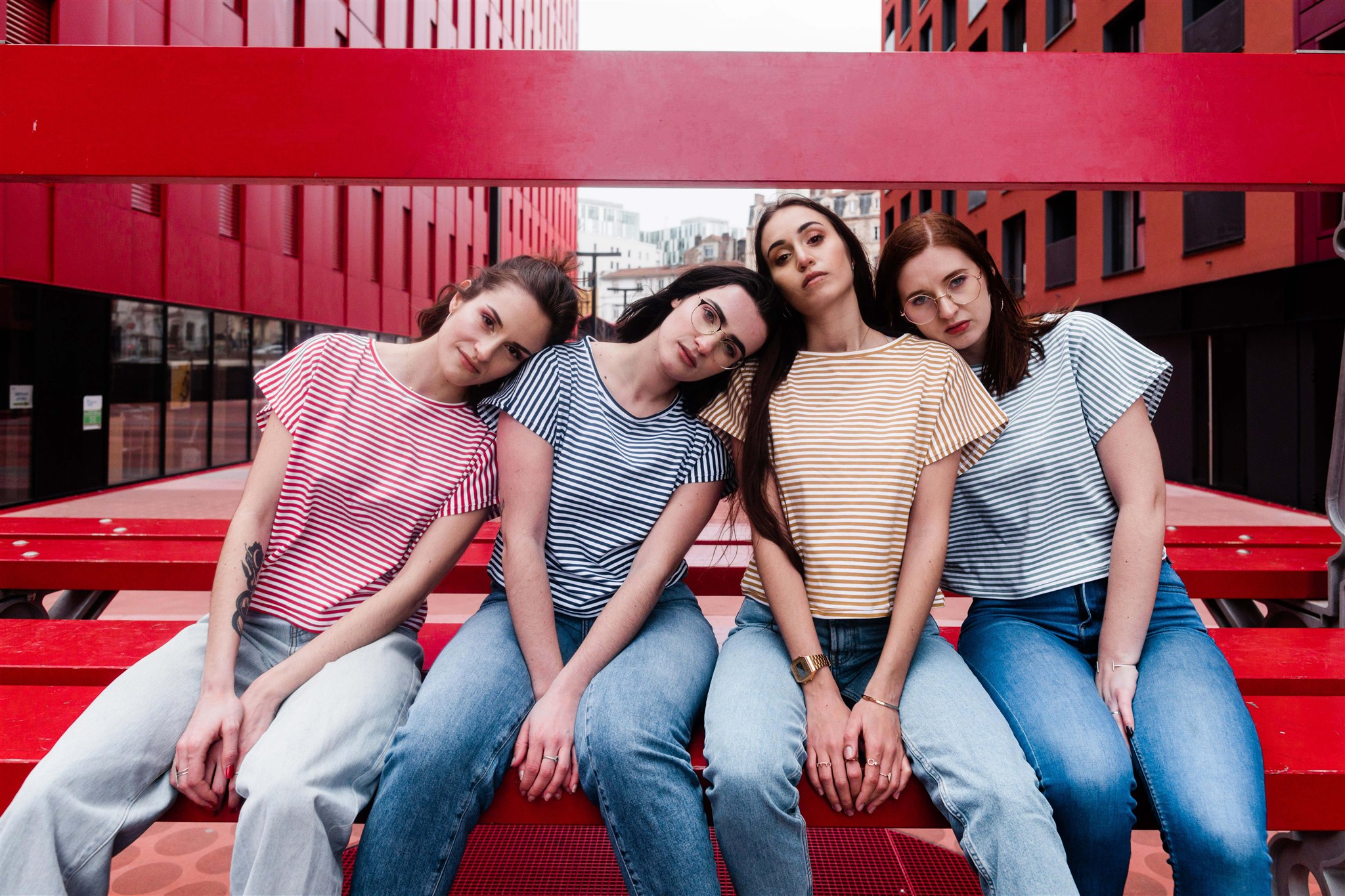 quatre filles assisent sur un banc la tête sur l'épaule de la voisine. Tshirt marinière et jean